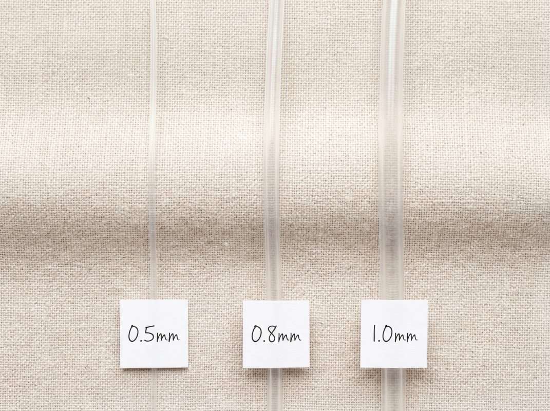 Flat lay thickness comparison of 0.5mm, 0.8mm, and 1.0mm clear elastic cord for bracelet making.