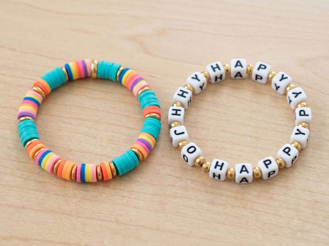 Two finished beginner beaded bracelets made with clay and letter beads, highlighting a secure surgeon's knot tied with elastic cord.